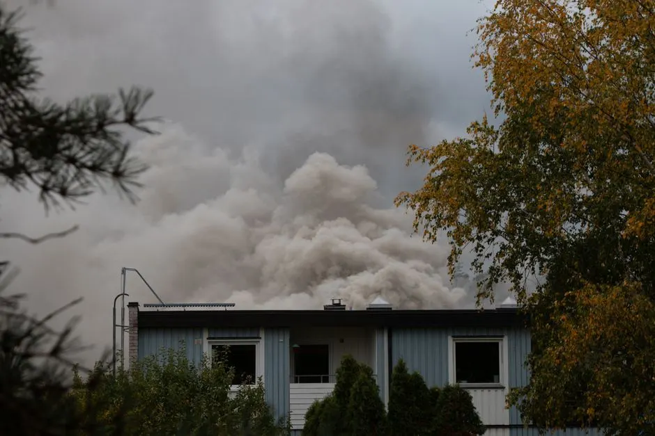 Thick smoke billows from a house fire in Stockholm, surrounded by trees.